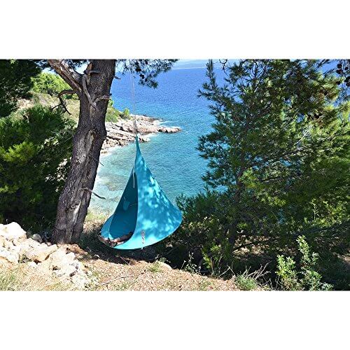 Anwendungsbeispiel - ein Junge liegt in einem blauen Hängezelt das an einem Baum befestigt ist der an einer Klippe steht - im Hintergrund sind Felsen und das Meer zu sehen - Foto aus einer anderen Perspektive Nr.2