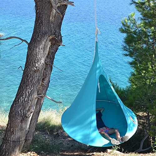 Anwendungsbeispiel - ein Junge liegt in einem blauen Hängezelt das an einem Baum befestigt ist der an einer Klippe steht - im Hintergrund sind Felsen und das Meer zu sehen - Foto aus einer anderen Perspektive